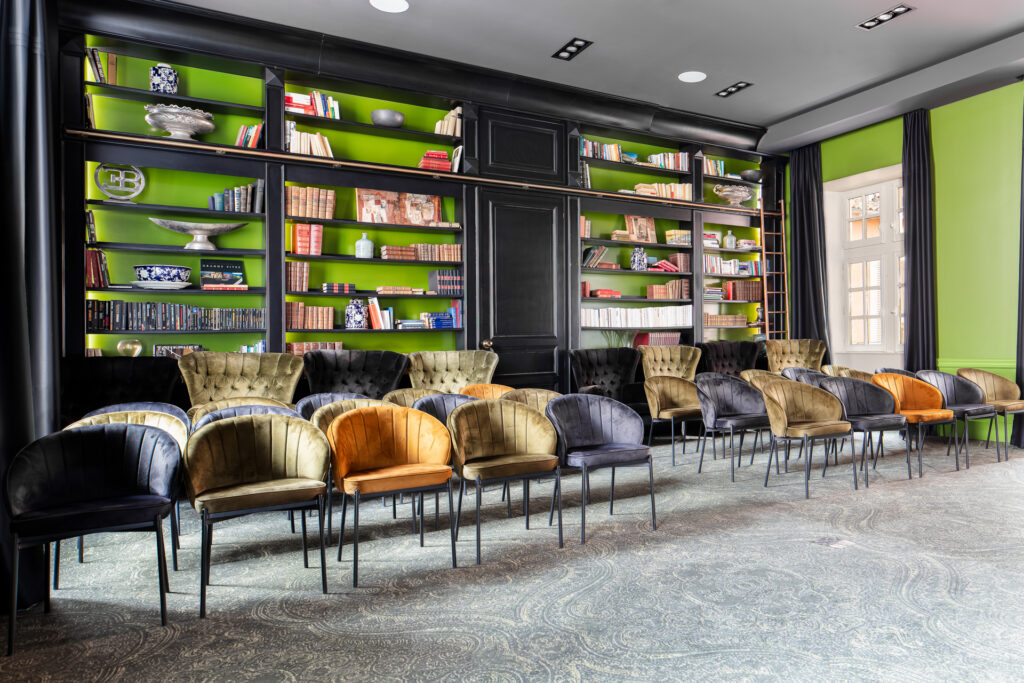 Rangées de fauteuils en velours devant une grande bibliothèque noire aux fonds verts à La Cour des Consuls.