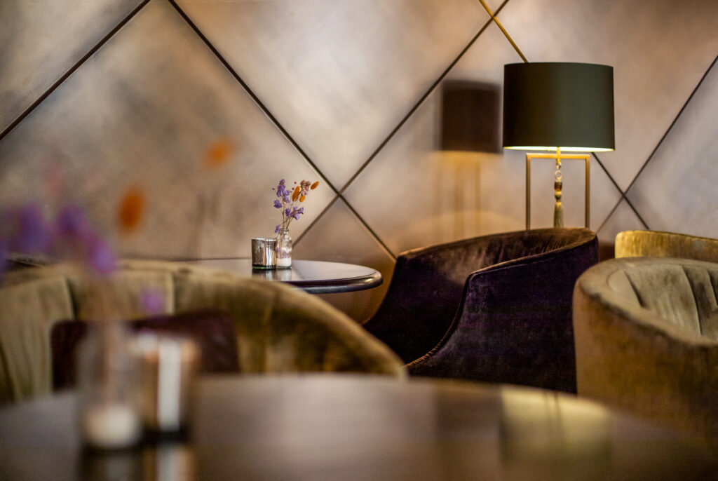 Fauteuils en velours, petite table fleurie et lampe à abat-jour sombre dans l’ambiance feutrée du bar Le 46.