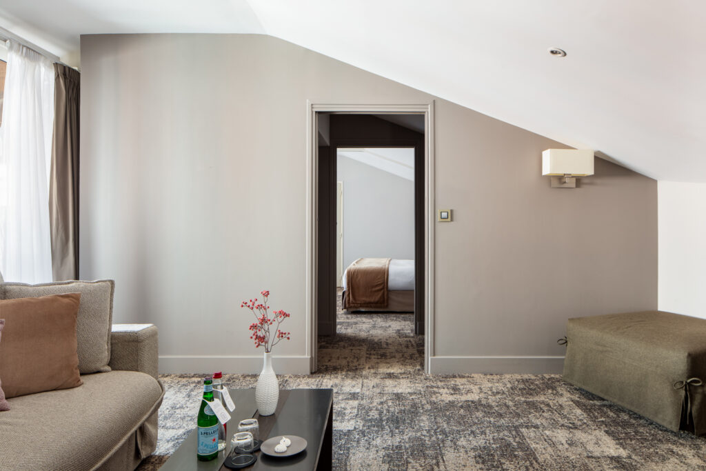 Salon aux tons beiges avec canapé et table basse, ouvrant sur une chambre à La Cour des Consuls.
