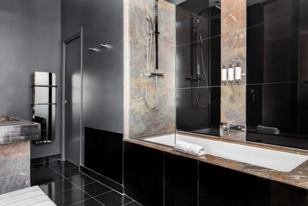 Salle de bains avec baignoire, pare-douche vitré et marbre gris et rosé associé à des surfaces noires.