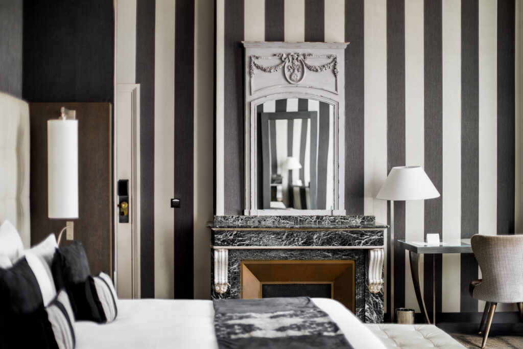 Cheminée en marbre et miroir face au lit, dans une chambre aux murs rayés gris et blanc.