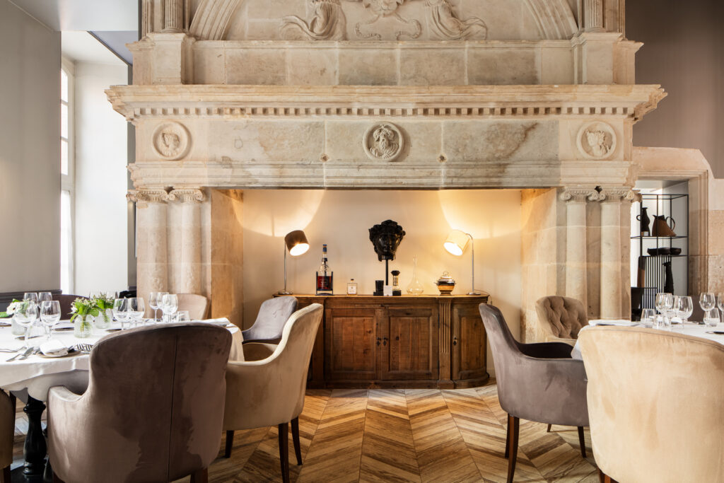 Cheminée monumentale en pierre sculptée derrière les tables dressées du restaurant de La Cour des Consuls.