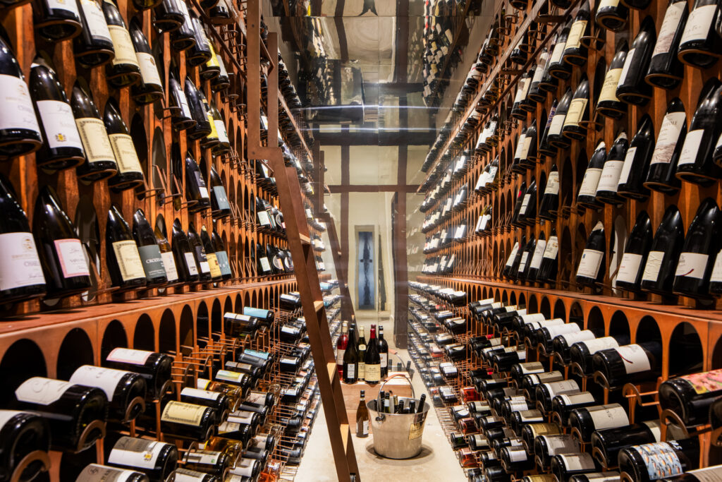 Allée étroite de la cave à vins, bordée de casiers en bois remplis de bouteilles de part et d’autre.